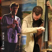 Zwei Musiker, einer mit Klarinette und der andere mit Kontrabass, performen auf einer B&uuml;hne. Im Hintergrund sind bunte Vorh&auml;nge zu sehen., &copy; links im Bild