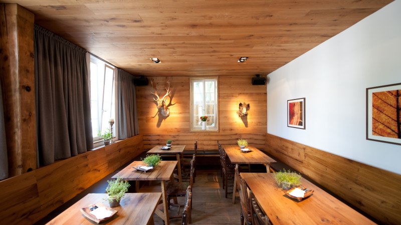 Ein gemütliches Restaurant mit Holztischen, Pflanzen auf den Tischen und dekorativen Elementen an den Wänden. Holzwände und -decke schaffen eine warme Atmosphäre., © Ruthenberg&Schlatter GbR Ein gemütliches Restaurant mit Holztischen, Pflanzen auf den Tischen und dekorativen Elementen an den Wänden. Holzwände und -decke schaffen eine warme Atmosphäre., © Ruthenberg&Schlatter GbR