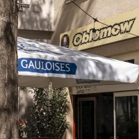 Eingang eines Caf&eacute;s namens Oblamow mit Gauloises-Sonnenschirm und Pflanzen. Au&szlig;enbeleuchtung und Schilder von Franziskaner und San Miguel sichtbar., &copy; SMG, Sarah Schmid