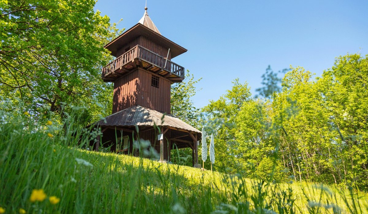 Holzturm auf Wiese, umgeben von Bäumen und Blumen, unter blauem Himmel., © Stadt Gaildorf Holzturm auf Wiese, umgeben von Bäumen und Blumen, unter blauem Himmel., © Stadt Gaildorf