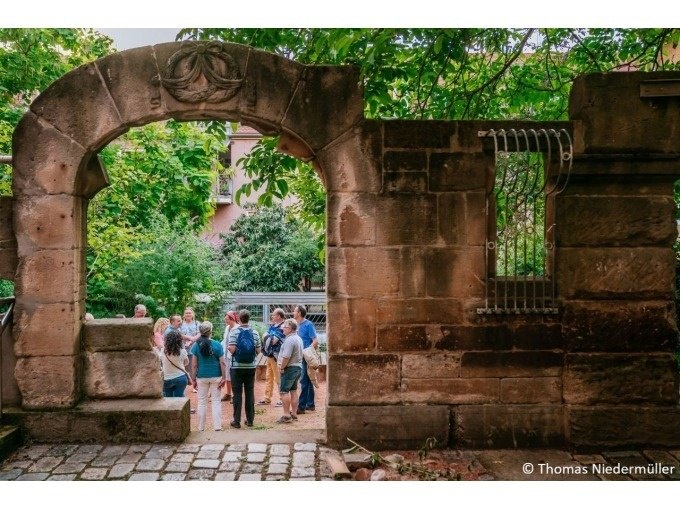 Gruppe von Menschen in einem Garten, umgeben von B&auml;umen, hinter einem alten Steintor mit dekorativem Bogen., &copy; Stuttgart Marketing GmbH