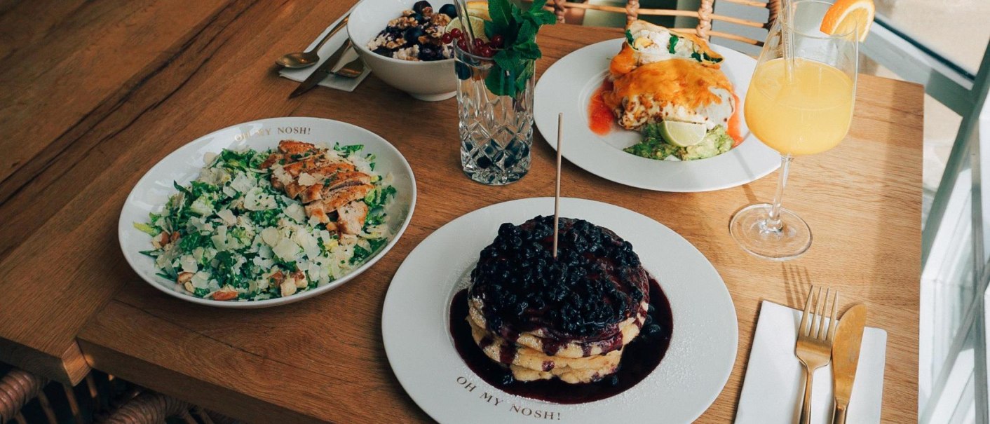 Ein Tisch mit Salat, Pfannkuchen mit Beeren, einem Getränk und weiteren Speisen auf Holztisch., © The Gardeners Nosh, Stuttgart Ein Tisch mit Salat, Pfannkuchen mit Beeren, einem Getränk und weiteren Speisen auf Holztisch., © The Gardeners Nosh, Stuttgart