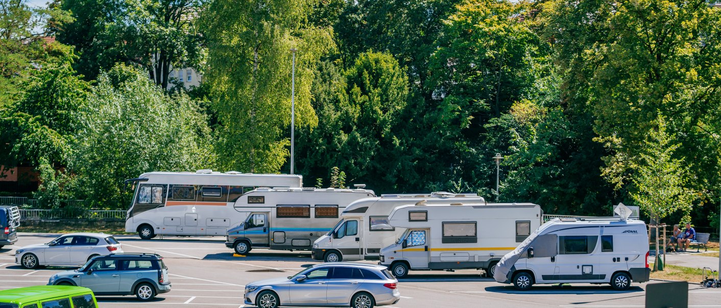 Wohnmobilstellplatz mit mehreren Wohnmobilen und Autos, umgeben von grünen Bäumen und blauem Himmel., © SMG, Thomas Niedermüller Wohnmobilstellplatz mit mehreren Wohnmobilen und Autos, umgeben von grünen Bäumen und blauem Himmel., © SMG, Thomas Niedermüller