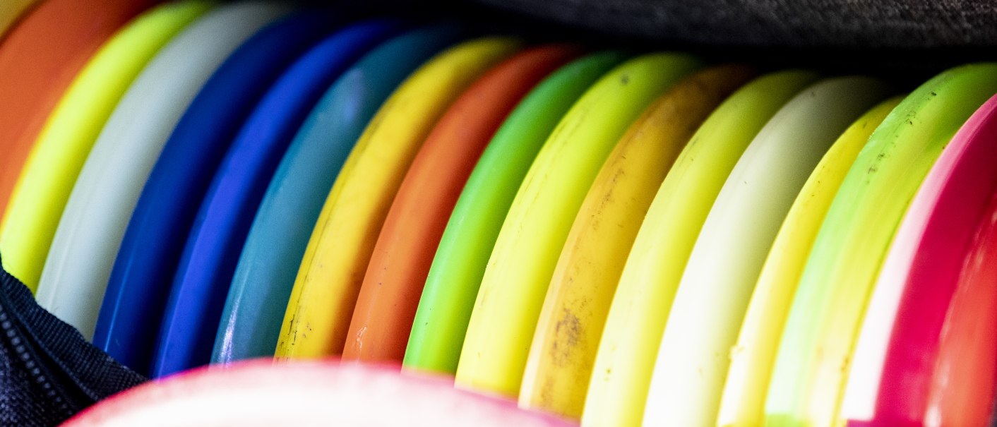 Bunte Discgolf-Scheiben in einer Tasche, eng aneinandergereiht. Die Farben reichen von Rot über Blau bis Gelb und Grün., © Benjamin Lau