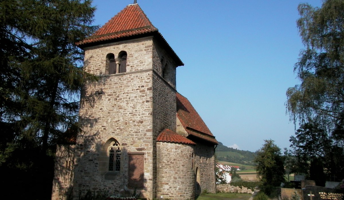 Romanische Kirche mit rotem Ziegeldach und Glockenturm, umgeben von Bäumen und Landschaft. Der Himmel ist klar und blau., © Tourismusgemeinschaft Marbach-Bottwartal