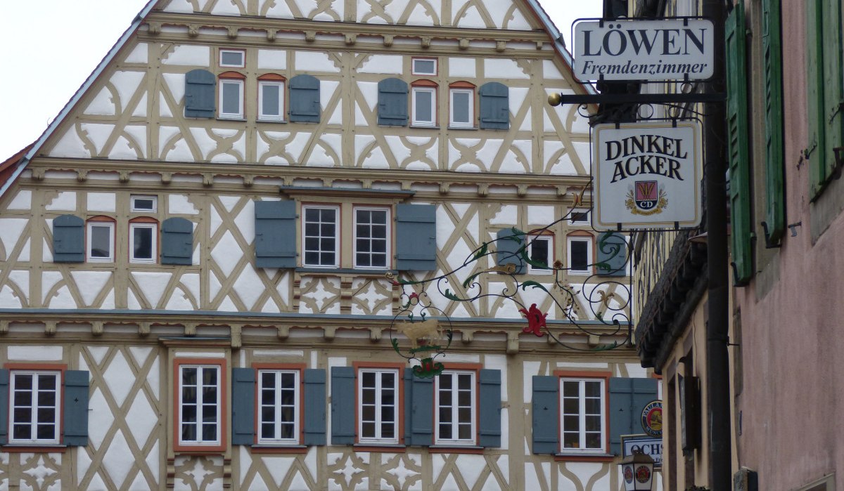 Fachwerkhaus in Enzweihingen mit blauen Fensterläden. Schilder für 'Löwen Fremdenzimmer' und 'Dinkel Acker' sind sichtbar., © Land der 1000 Hügel - Kraichgau-Stromberg