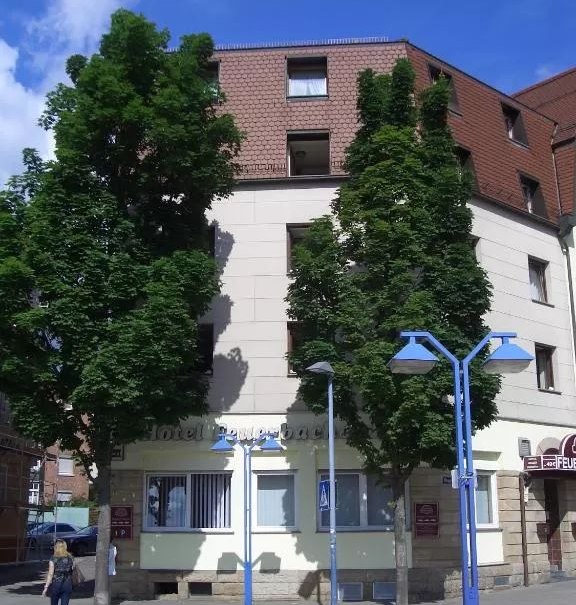 Das Hotel Feuerbacher Hof mit Bäumen davor und blauen Straßenlaternen. Eine Person überquert den Zebrastreifen., © Feuerbacher Hof Das Hotel Feuerbacher Hof mit Bäumen davor und blauen Straßenlaternen. Eine Person überquert den Zebrastreifen., © Feuerbacher Hof