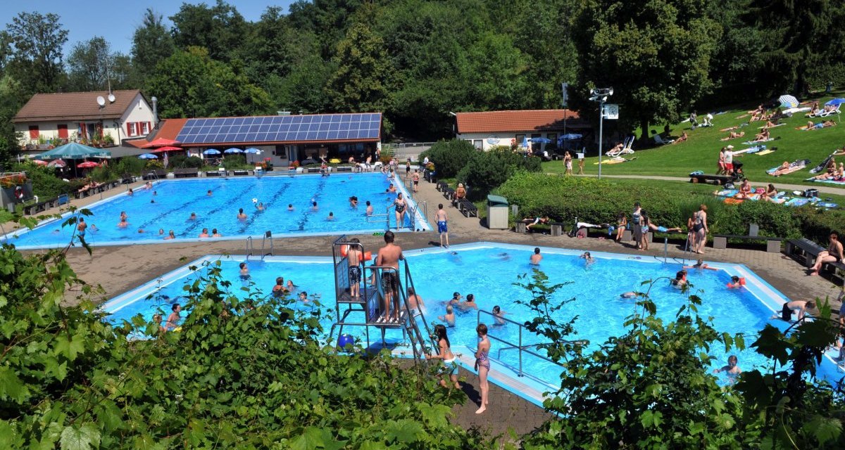 Ein Freibad mit vielen Besuchern im Wasser und auf der Liegewiese. Im Hintergrund sind Bäume und ein Gebäude mit Solarpanelen zu sehen., © Gemeinde Bad Boll Ein Freibad mit vielen Besuchern im Wasser und auf der Liegewiese. Im Hintergrund sind Bäume und ein Gebäude mit Solarpanelen zu sehen., © Gemeinde Bad Boll