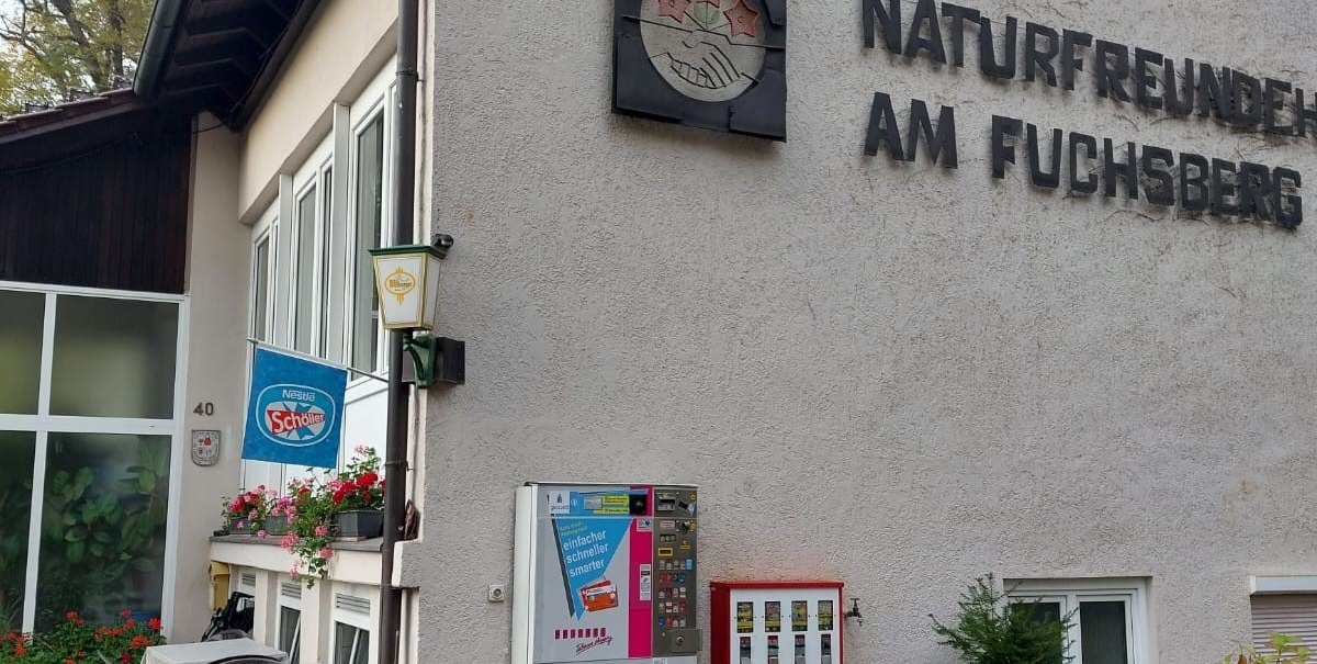 Gebäude mit der Aufschrift 'Naturfreunde am Fuchsberg', Tisch und Stühle draußen, Getränkeautomat an der Wand., © Naturfreunde Sindelfingen Gebäude mit der Aufschrift 'Naturfreunde am Fuchsberg', Tisch und Stühle draußen, Getränkeautomat an der Wand., © Naturfreunde Sindelfingen