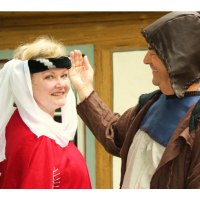 Zwei Personen in mittelalterlicher Kleidung l&auml;cheln vor einem Fachwerkhaus. Die Frau tr&auml;gt ein rotes Gewand, der Mann eine braune Kapuze., &copy; Touristik und Marketing GmbH