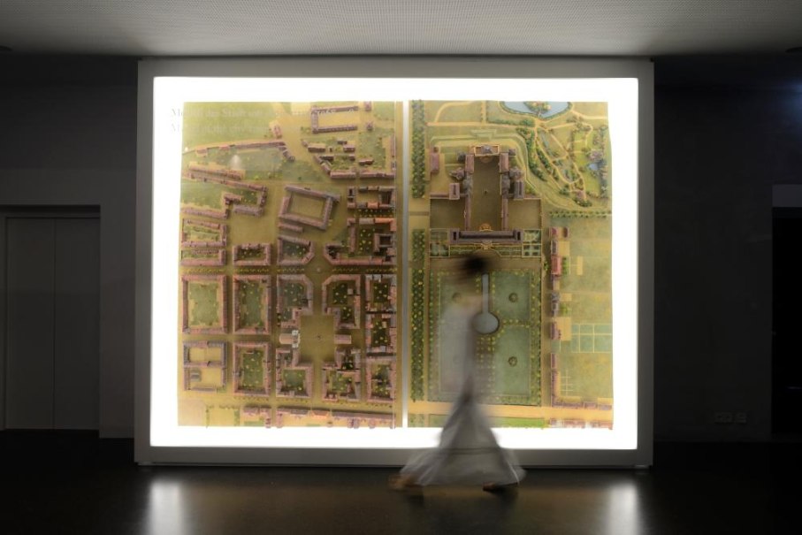 Eine Person bewegt sich vor einem beleuchteten Stadtplan im Museumsfoyer. Die Karte zeigt detaillierte Geb&auml;ude und Gr&uuml;nfl&auml;chen., &copy; Ludwigsburg Museum