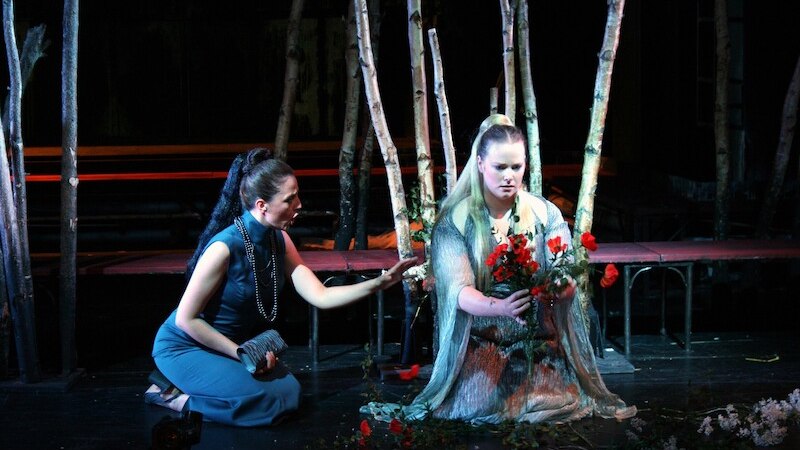 Zwei Frauen in einem dramatischen Moment auf der Bühne. Eine kniet mit Blumen in der Hand, die andere sitzt daneben. Im Hintergrund stehen Baumstämme., © Touristik Bad Wildbad GmbH Zwei Frauen in einem dramatischen Moment auf der Bühne. Eine kniet mit Blumen in der Hand, die andere sitzt daneben. Im Hintergrund stehen Baumstämme., © Touristik Bad Wildbad GmbH