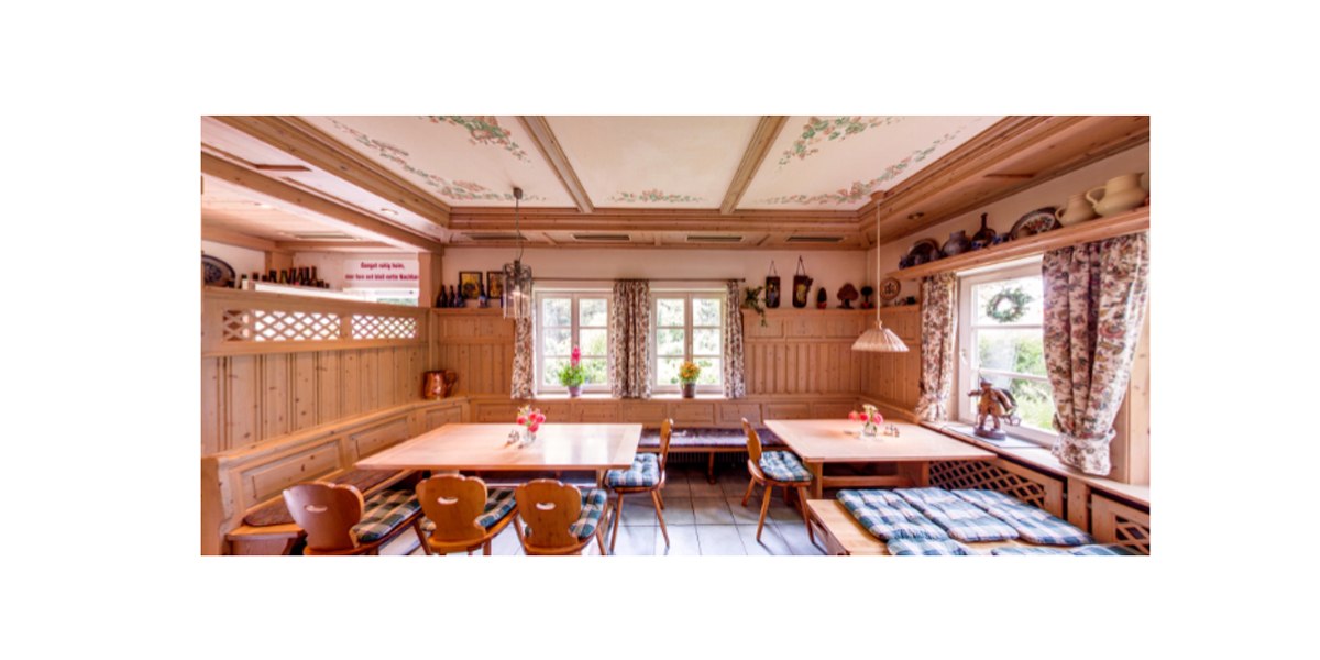 Ein gemütlicher Gastraum mit Holzmöbeln, karierten Sitzpolstern und floralen Vorhängen. An der Decke sind Blumenmuster, auf Regalen stehen Keramiken., © Weingut Karl Wöhrwag