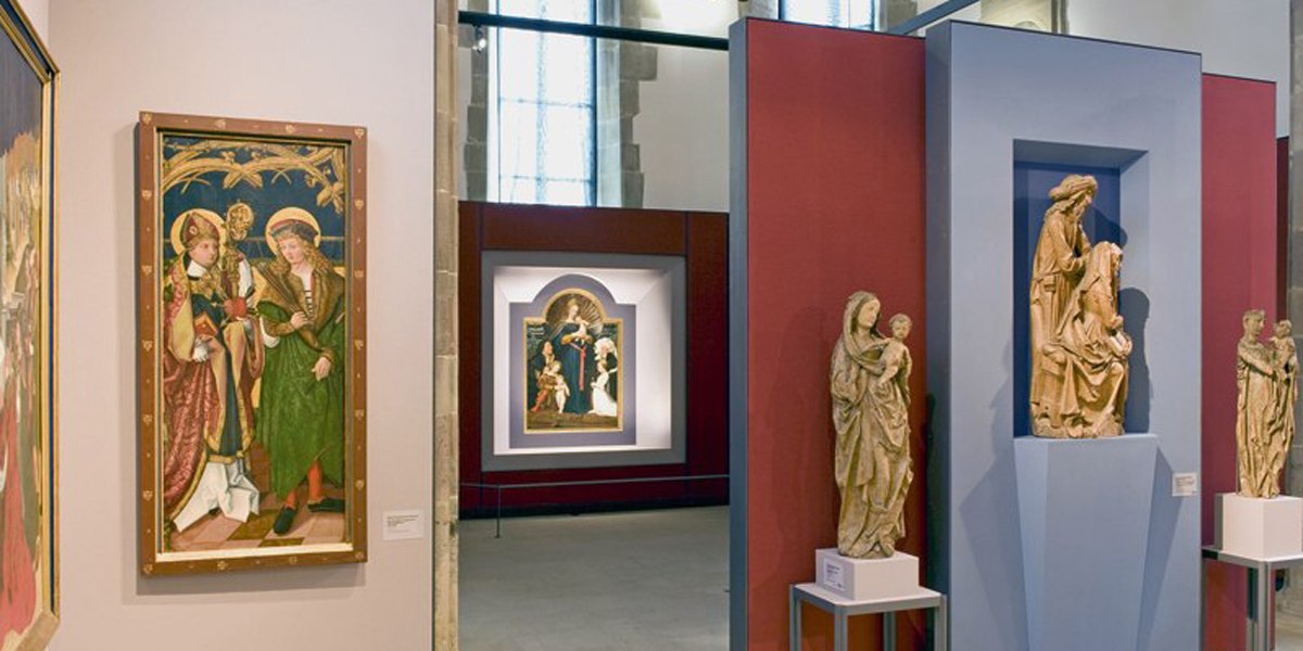 Innenansicht der Johanniterkirche Schwäbisch Hall mit Gemälden und Skulpturen auf roten und blauen Wänden ausgestellt., © Andi Schmid