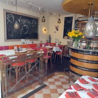 Ein gemütliches Restaurant mit Tafeln, gelben Blumen und gedeckten Tischen. Der Schriftzug 'V Bandits' ist auf einer Tafel zu sehen., © Lisa Bakavos V-Bandits Ein gemütliches Restaurant mit Tafeln, gelben Blumen und gedeckten Tischen. Der Schriftzug 'V Bandits' ist auf einer Tafel zu sehen., © Lisa Bakavos V-Bandits