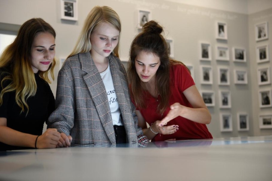 Drei junge Frauen stehen in einem Museum und betrachten interessiert eine Ausstellung. Im Hintergrund sind gerahmte Fotos an der Wand zu sehen., © Ludwigsburg Museum Drei junge Frauen stehen in einem Museum und betrachten interessiert eine Ausstellung. Im Hintergrund sind gerahmte Fotos an der Wand zu sehen., © Ludwigsburg Museum