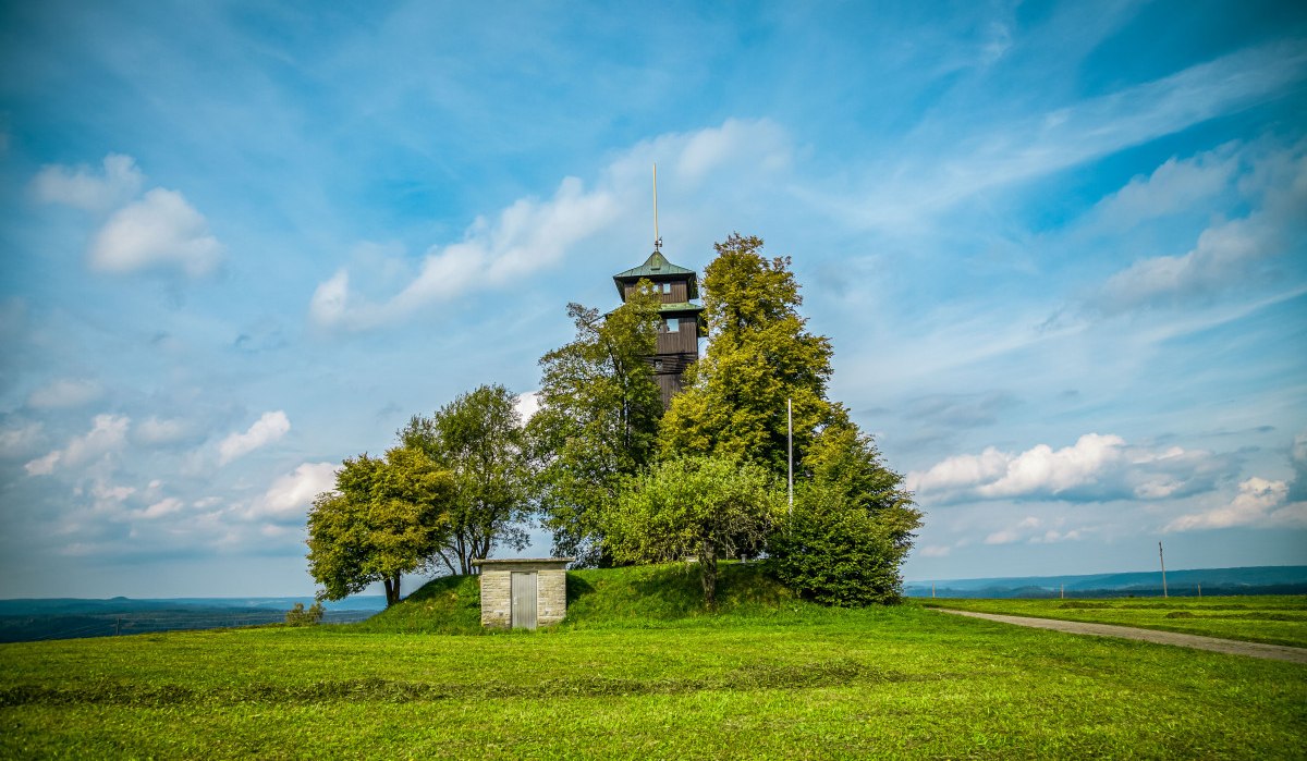 Der Hagbergturm in Gschwend steht auf einem Hügel, umgeben von Bäumen und einer grünen Wiese. Ein kleiner Weg führt zum Turm, der Himmel ist blau mit Wolken., © agentur arcos/Niki Eilers Der Hagbergturm in Gschwend steht auf einem Hügel, umgeben von Bäumen und einer grünen Wiese. Ein kleiner Weg führt zum Turm, der Himmel ist blau mit Wolken., © agentur arcos/Niki Eilers