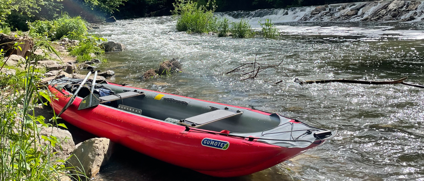 Rotes Kanu am Flussufer, umgeben von Pflanzen. Im Hintergrund fließt der Fluss mit kleinem Wasserfall., © seezeit GmbH Rotes Kanu am Flussufer, umgeben von Pflanzen. Im Hintergrund fließt der Fluss mit kleinem Wasserfall., © seezeit GmbH