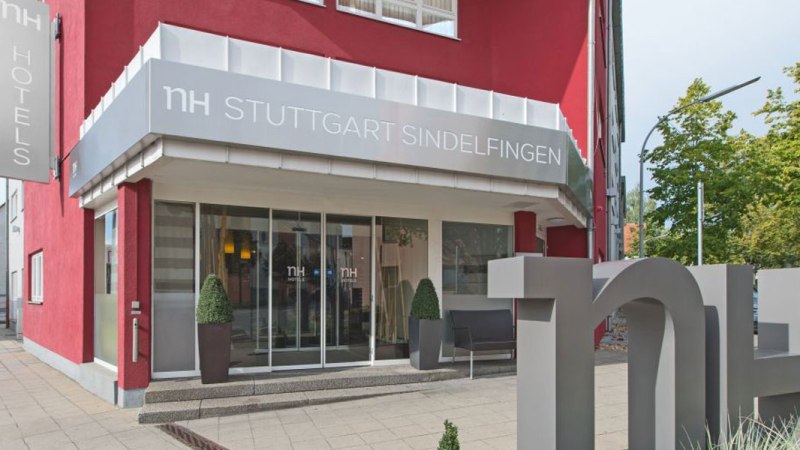Eingang des NH Hotels in Sindelfingen mit roter Fassade, großem Logo und Pflanzen vor der Tür., © NH Stuttgart Sindelfingen Eingang des NH Hotels in Sindelfingen mit roter Fassade, großem Logo und Pflanzen vor der Tür., © NH Stuttgart Sindelfingen