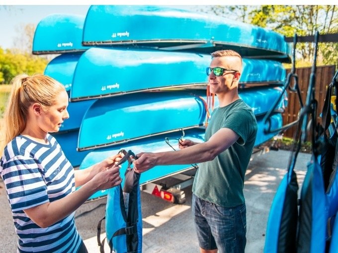 Zwei Personen stehen vor einem Stapel blauer Kanus. Sie halten Schwimmwesten und bereiten sich auf eine Kanutour vor., © Cool-Tours StattReisen Zwei Personen stehen vor einem Stapel blauer Kanus. Sie halten Schwimmwesten und bereiten sich auf eine Kanutour vor., © Cool-Tours StattReisen