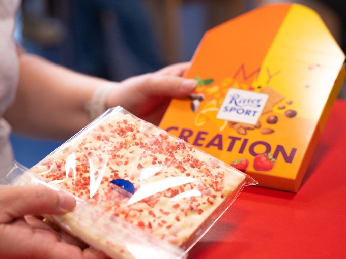 Person hält eine Tafel weiße Schokolade mit roten Streuseln und eine Verpackung mit 'My Creation' von Ritter Sport., © Alfred Ritter GmbH & Co. KG | Waldenbuch Person hält eine Tafel weiße Schokolade mit roten Streuseln und eine Verpackung mit 'My Creation' von Ritter Sport., © Alfred Ritter GmbH & Co. KG | Waldenbuch
