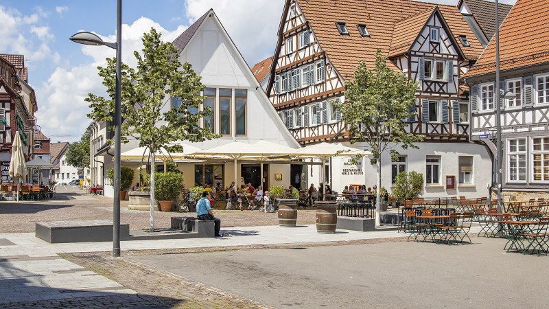 Fachwerkhäuser in Kirchheim unter Teck mit Straßencafé und Bäumen. Menschen sitzen draußen, genießen das Wetter. Historische Architektur und gemütliche Atmosphäre., © Torsten Wenzler Fachwerkhäuser in Kirchheim unter Teck mit Straßencafé und Bäumen. Menschen sitzen draußen, genießen das Wetter. Historische Architektur und gemütliche Atmosphäre., © Torsten Wenzler