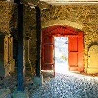 Ein historischer Durchgang mit Grabsteinen an den Wänden und einem roten Tor, das nach draußen führt. Sonnenlicht fällt durch das Tor auf den Boden., © Stuttgart-Marketing GmbH, Sarah Schmid Ein historischer Durchgang mit Grabsteinen an den Wänden und einem roten Tor, das nach draußen führt. Sonnenlicht fällt durch das Tor auf den Boden., © Stuttgart-Marketing GmbH, Sarah Schmid