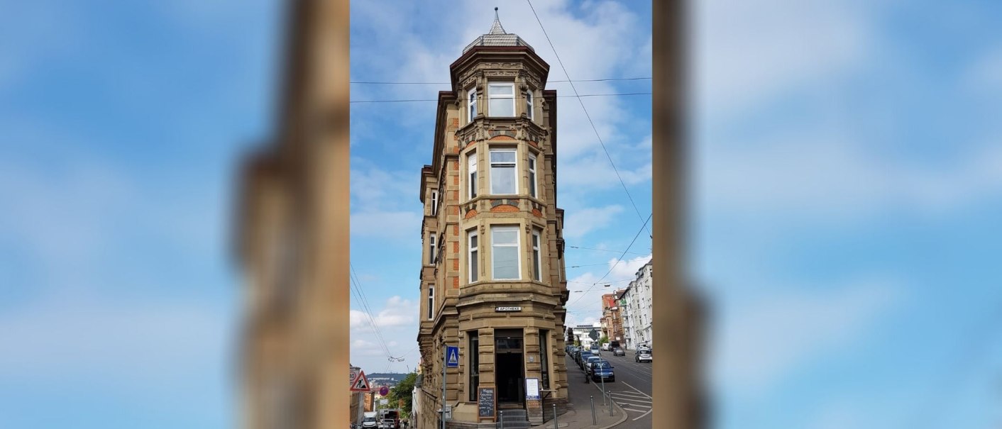 Historisches Eckgebäude mit Apotheke im Erdgeschoss, umgeben von Straßen und Autos, unter blauem Himmel., © SMG