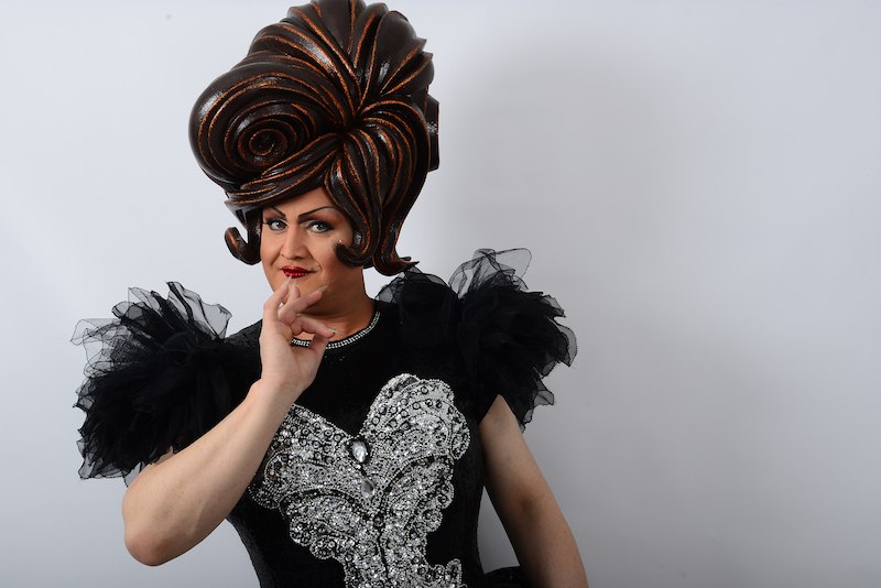 Person mit großer, kunstvoller Perücke und schwarzem Kleid mit silbernen Verzierungen posiert vor weißem Hintergrund., © Kurverwaltung Bad Urach