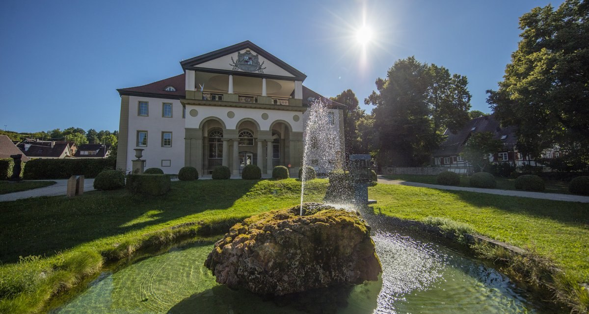 Schloss Dätzingen mit einem Springbrunnen im Vordergrund. Die Sonne scheint hell am blauen Himmel, umgeben von grünen Bäumen und gepflegtem Rasen., © Stuttgart Marketing GmbH Schloss Dätzingen mit einem Springbrunnen im Vordergrund. Die Sonne scheint hell am blauen Himmel, umgeben von grünen Bäumen und gepflegtem Rasen., © Stuttgart Marketing GmbH