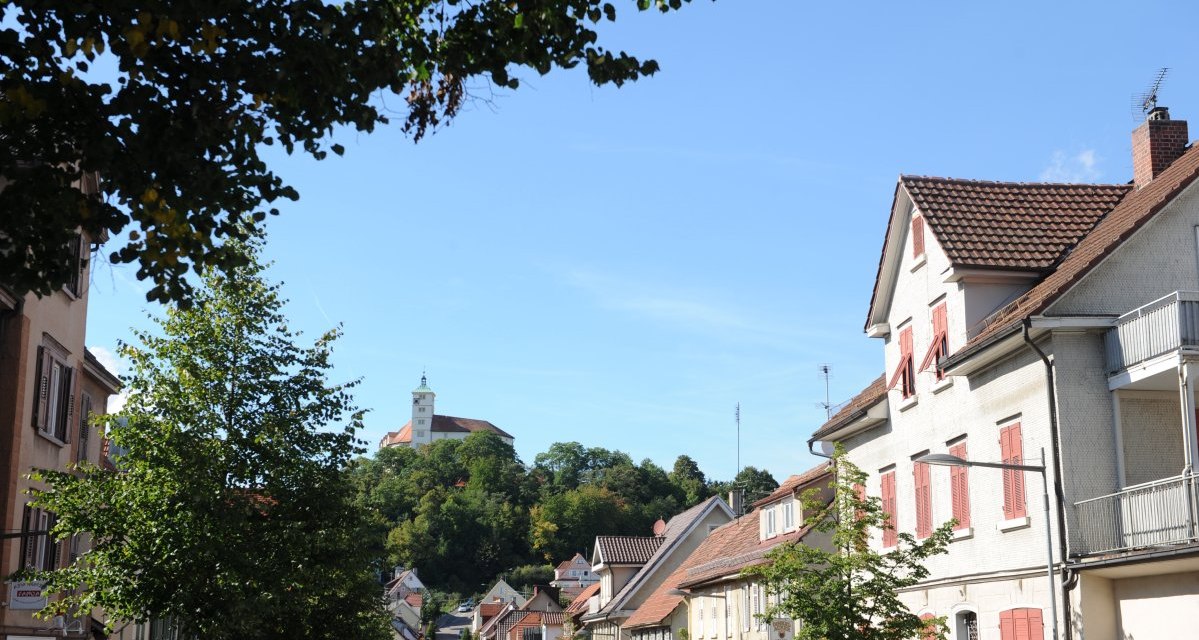 Eine Straße mit Häusern und Bäumen, im Hintergrund ein Schloss auf einem bewaldeten Hügel unter blauem Himmel., © Land der 1000 Hügel - Kraichgau-Stromberg Eine Straße mit Häusern und Bäumen, im Hintergrund ein Schloss auf einem bewaldeten Hügel unter blauem Himmel., © Land der 1000 Hügel - Kraichgau-Stromberg