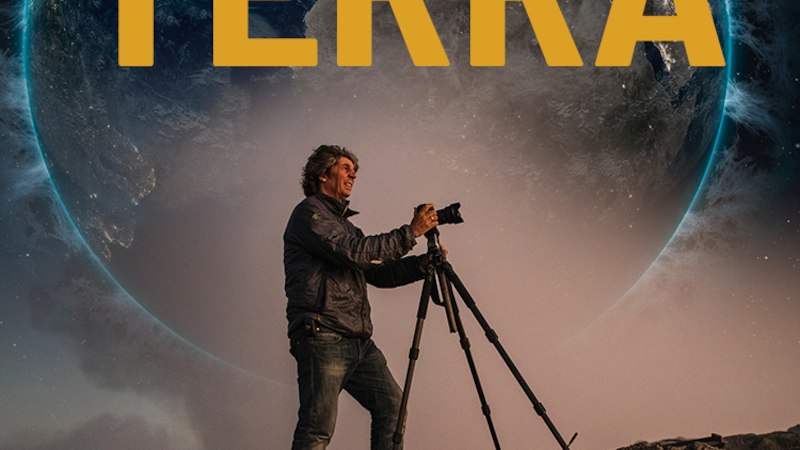 Ein Fotograf mit Kamera und Stativ steht vor einem großen Bild der Erde. Der Schriftzug 'TERRA' ist prominent zu sehen., © Expedition Erde