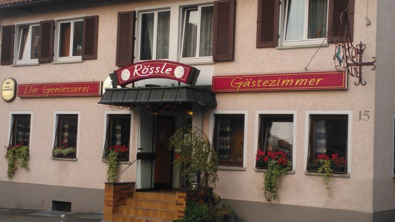 Gasthaus Rössle in Urbach mit Schildern 'Die Geniesserei' und 'Gästezimmer', Blumenkästen an den Fenstern und einer Eingangstreppe., © Gasthaus Rössle