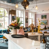 Gem&uuml;tliches Caf&eacute; mit Blumen und Brezeln auf der Theke, blauen Sofas und Kunst an den W&auml;nden. Gro&szlig;e Fenster lassen viel Licht herein., &copy; SMG, Sarah Schmid