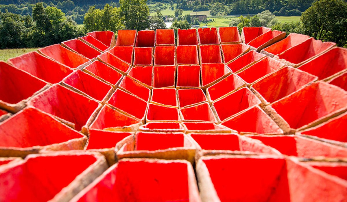 Rote, geometrische Struktur in Form eines Kraters vor einer grünen Landschaft mit Bäumen und Hügeln im Hintergrund., © Natur.Nah. Schönbuch & Heckengäu