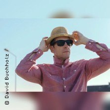 Person mit Strohhut und Sonnenbrille blickt in die Ferne, vor einem klaren blauen Himmel., &copy; links im Bild