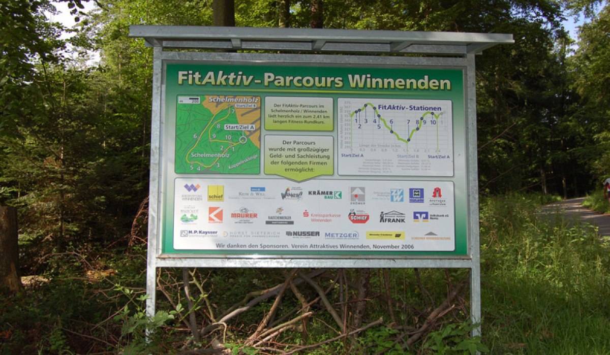 Schild des FitAktiv-Parcours Winnenden im Wald. Es zeigt eine Karte des Parcours und Logos von Sponsoren. Der Weg führt durch bewaldetes Gebiet., © Winnenden - Stuttgart-Marketing GmbH Schild des FitAktiv-Parcours Winnenden im Wald. Es zeigt eine Karte des Parcours und Logos von Sponsoren. Der Weg führt durch bewaldetes Gebiet., © Winnenden - Stuttgart-Marketing GmbH
