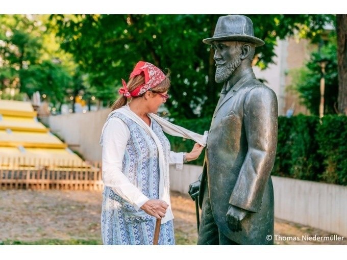 Frau mit Kopftuch zieht spielerisch an der Krawatte einer Bronzestatue in einem Park., &copy; Stuttgart Marketing GmbH