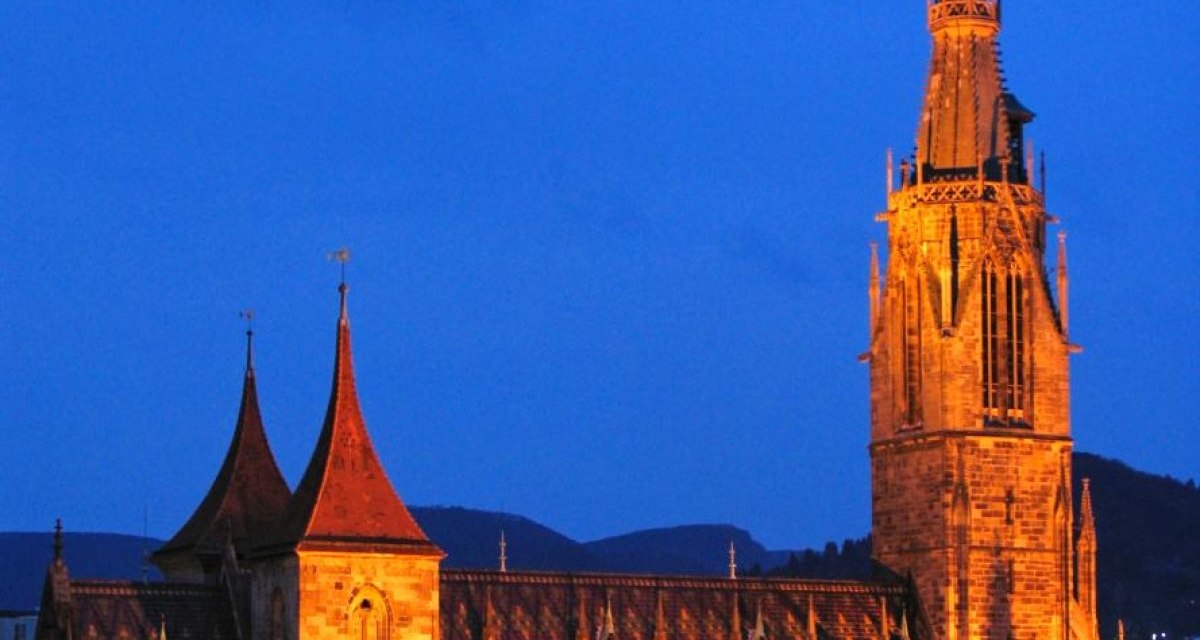 Eine beleuchtete Kirche in Reutlingen bei Nacht, umgeben von Häuserdächern. Der Himmel ist dunkelblau., © Mythos Schwäbische Alb im Landkreis Reutlingen e.V. Eine beleuchtete Kirche in Reutlingen bei Nacht, umgeben von Häuserdächern. Der Himmel ist dunkelblau., © Mythos Schwäbische Alb im Landkreis Reutlingen e.V.