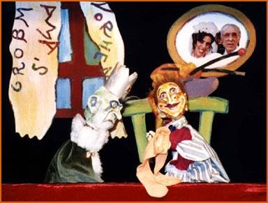 Zwei Handpuppen in einem Puppentheater. Eine Puppe tr&auml;gt eine Krone, die andere hat ein fr&ouml;hliches Gesicht. Im Hintergrund ein Fenster mit Vorh&auml;ngen., &copy; Bildrechte: Gregor Oehmann