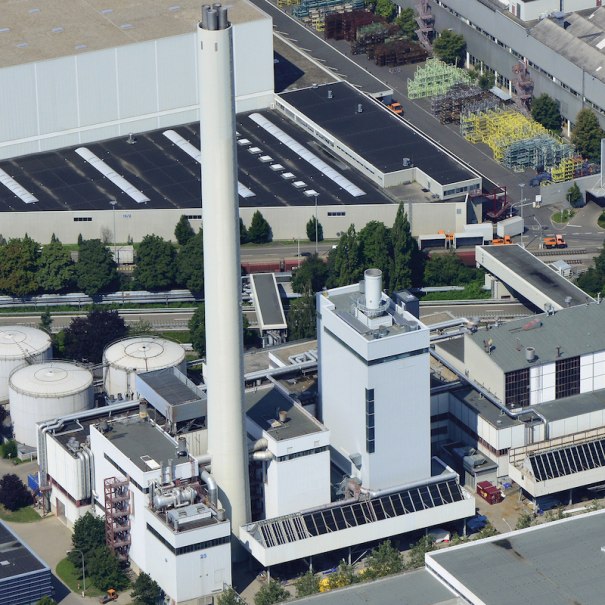 Luftaufnahme eines Industriekomplexes mit hohen Schornsteinen, mehreren Gebäuden und Tanks. Grünflächen und Straßen umgeben die Anlage., © Mercedes-Benz AG