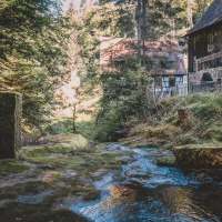 Ein Bach fließt durch einen Wald, vorbei an einem alten Fachwerkhaus. Moosbewachsene Steine und Bäume umgeben die Szene., © Stadt Welzheim Ein Bach fließt durch einen Wald, vorbei an einem alten Fachwerkhaus. Moosbewachsene Steine und Bäume umgeben die Szene., © Stadt Welzheim