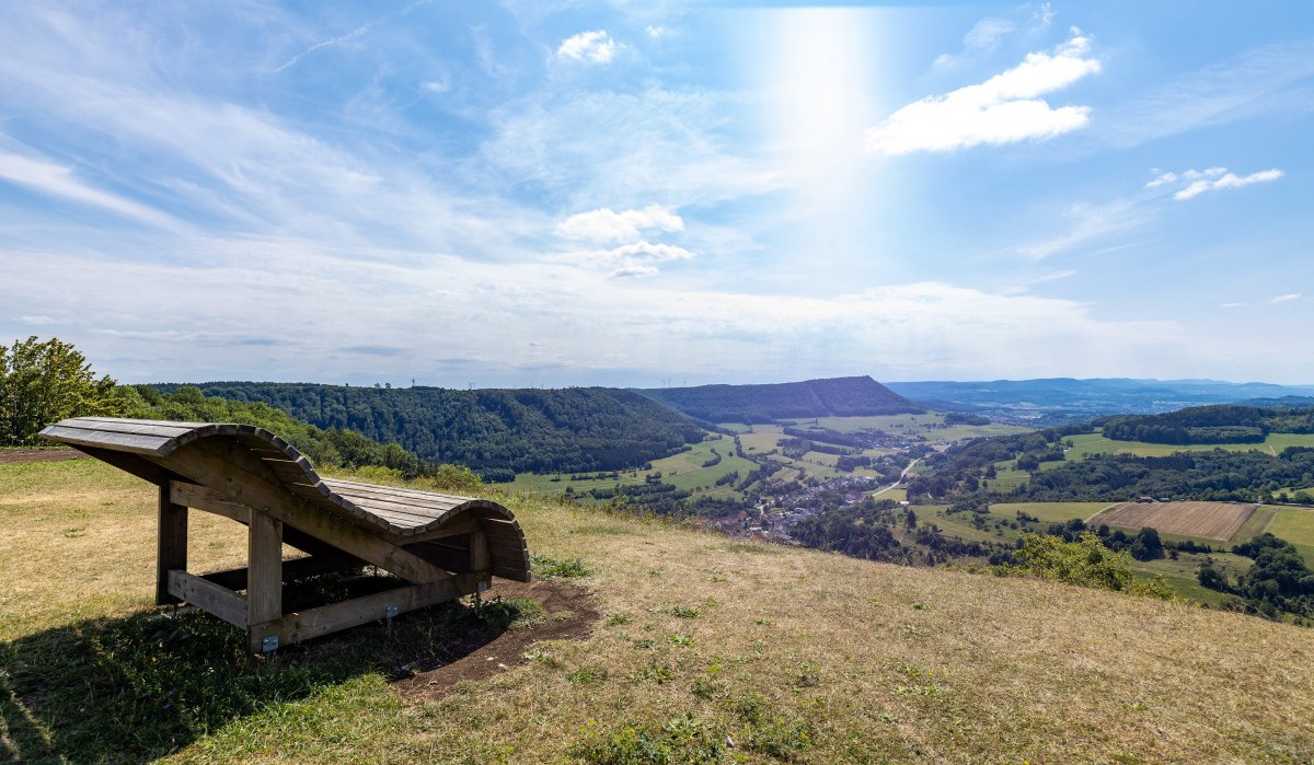 Holzliege am Aussichtspunkt mit Blick auf grüne Hügel und Täler unter blauem Himmel., © Foto Thomas Zehnder