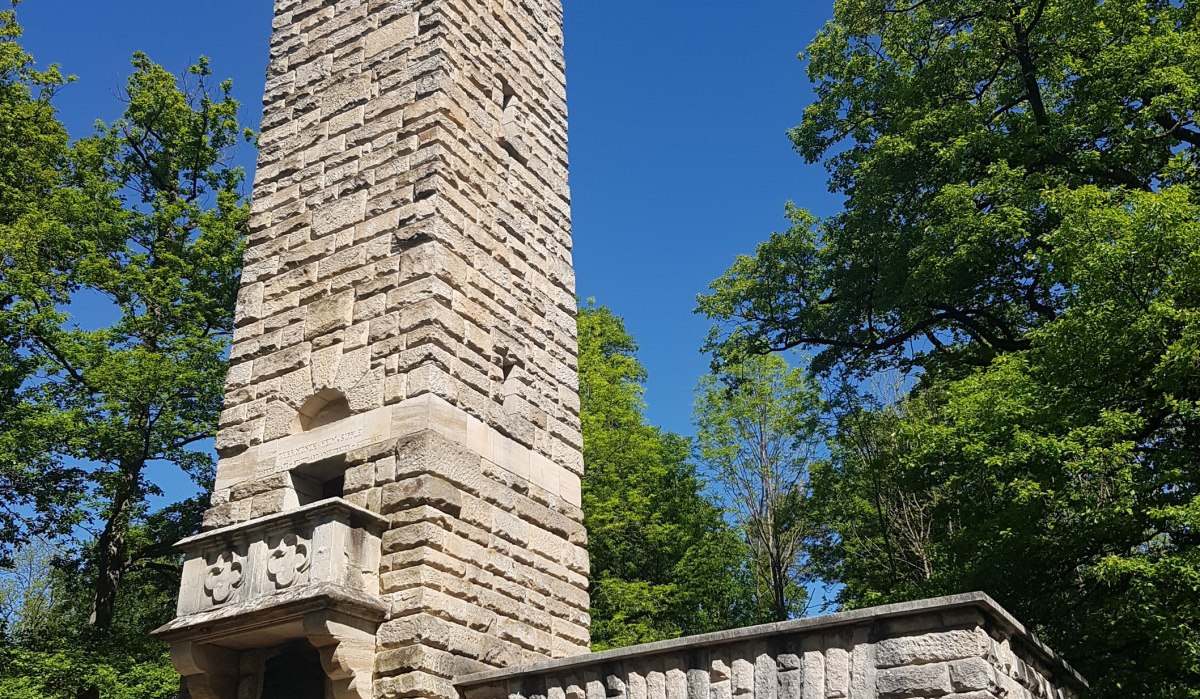 Der Kernenturm aus Stein erhebt sich vor einem klaren blauen Himmel, umgeben von grünen Bäumen. Im Vordergrund sind Stühle zu sehen., © Remstal Tourismus e.V. Der Kernenturm aus Stein erhebt sich vor einem klaren blauen Himmel, umgeben von grünen Bäumen. Im Vordergrund sind Stühle zu sehen., © Remstal Tourismus e.V.