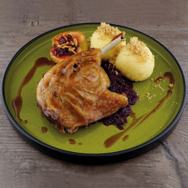 Gänsekeule mit Rotkohl, Knödeln und gefülltem Apfel auf grünem Teller, dekoriert mit Soße., © Mercedes-Benz AG Gänsekeule mit Rotkohl, Knödeln und gefülltem Apfel auf grünem Teller, dekoriert mit Soße., © Mercedes-Benz AG