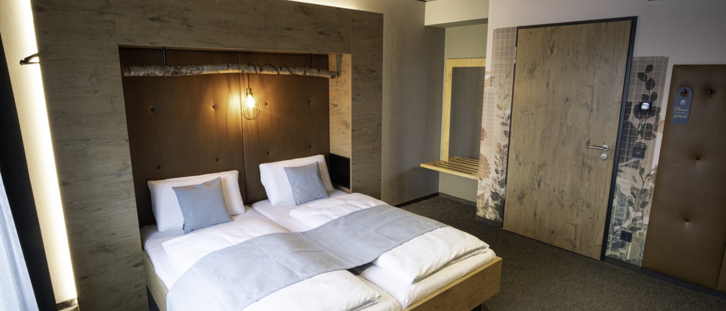 Modernes Doppelzimmer mit Holzverkleidung, gemütlichem Bett und stilvoller Beleuchtung. Dezente Farben und minimalistisches Design schaffen eine einladende Atmosphäre., © 13 6 Design GmbH (Judenhof 10, 89073 Ulm)