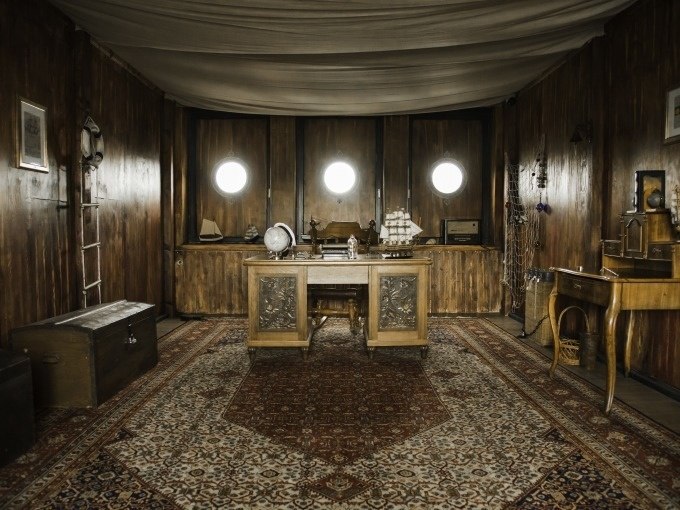 Rustikales Schiffsinterieur mit Holzwänden, Schreibtisch, Globus und Modellschiff. Drei Bullaugen an der Wand., © ExitGames Stuttgart Rustikales Schiffsinterieur mit Holzwänden, Schreibtisch, Globus und Modellschiff. Drei Bullaugen an der Wand., © ExitGames Stuttgart