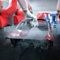 Industrieroboter lackieren eine Autokarosserie in einer Fabrikhalle. Die Roboterarme sind rot und sprühen Farbe auf das Fahrzeug., © Mercedes-Benz AG