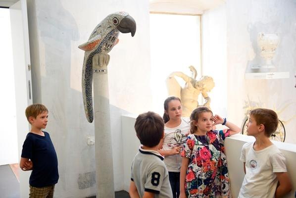Kinder stehen in einem Museum um eine bunte Papageienstatue und schauen interessiert., &copy; Ludwigsburg Museum