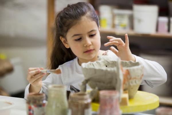 Ein Kind bemalt konzentriert eine Tonfigur in einem Workshop. Verschiedene Farbtöpfe stehen auf dem Tisch., © Kunstschule Labyrinth Ein Kind bemalt konzentriert eine Tonfigur in einem Workshop. Verschiedene Farbtöpfe stehen auf dem Tisch., © Kunstschule Labyrinth